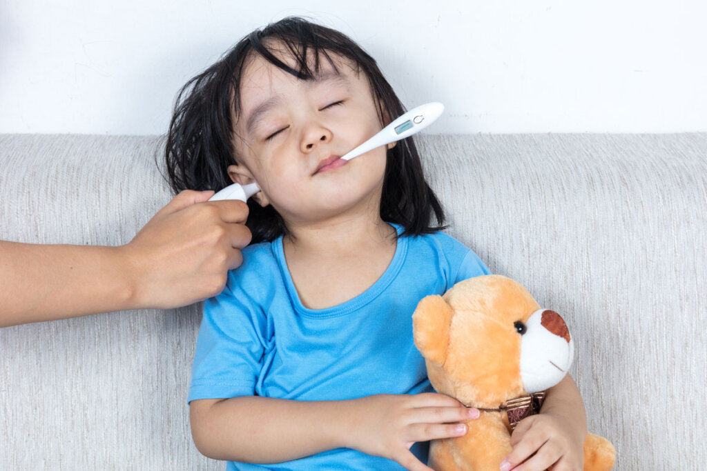 Niño con termómetro para la fiebre en el oído y la boca