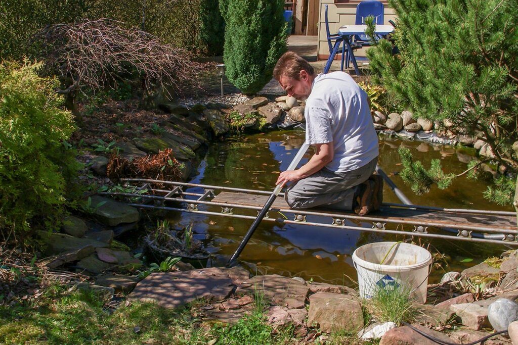 Un hombre limpia un estanque de jardín con un aspirador de barro